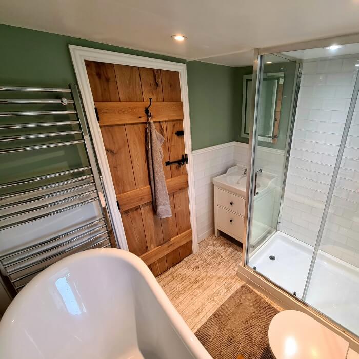 Oak internal door with black iron hinges and handle, installed in a bathroom with a modern bathtub and glass shower.